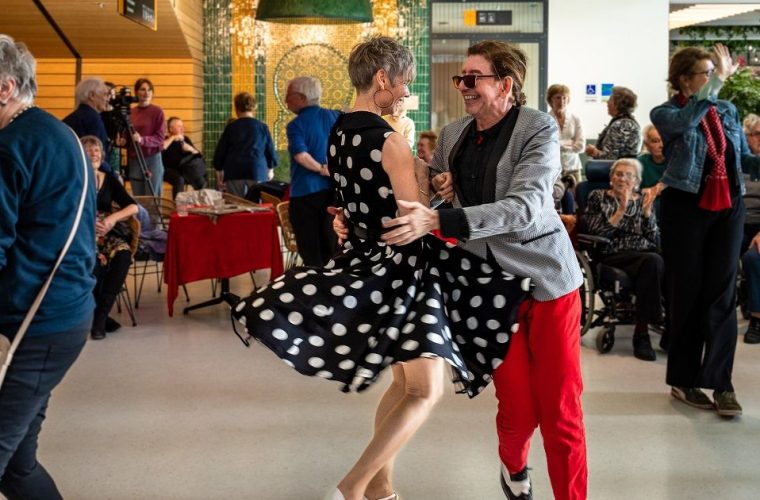 Groep ouderen danst samen op het Kunstenplein in Den Haag tijdens Het Danspaleis, omringd door sfeervolle live muziek